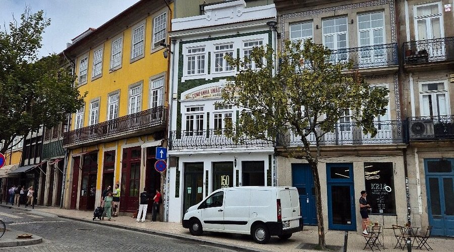 Fachada restaurada de um edifício histórico de três pisos em zona urbana, com janelas envidraçadas de caixilho branco e azulejos verdes na área central, integrando um novo revestimento leve em Light Steel Frame discretamente adaptado ao estilo tradicional.