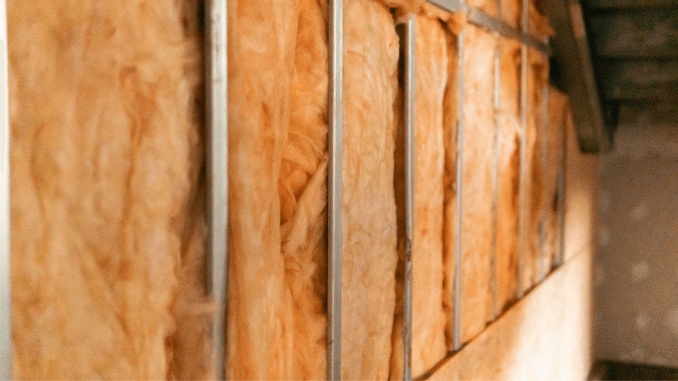 Vista em close-up de mantas de isolamento de cor laranja (lã mineral/lã de vidro) colocadas entre perfis metálicos verticais de uma estrutura Light Steel Frame (LSF), em obra, antes do revestimento.